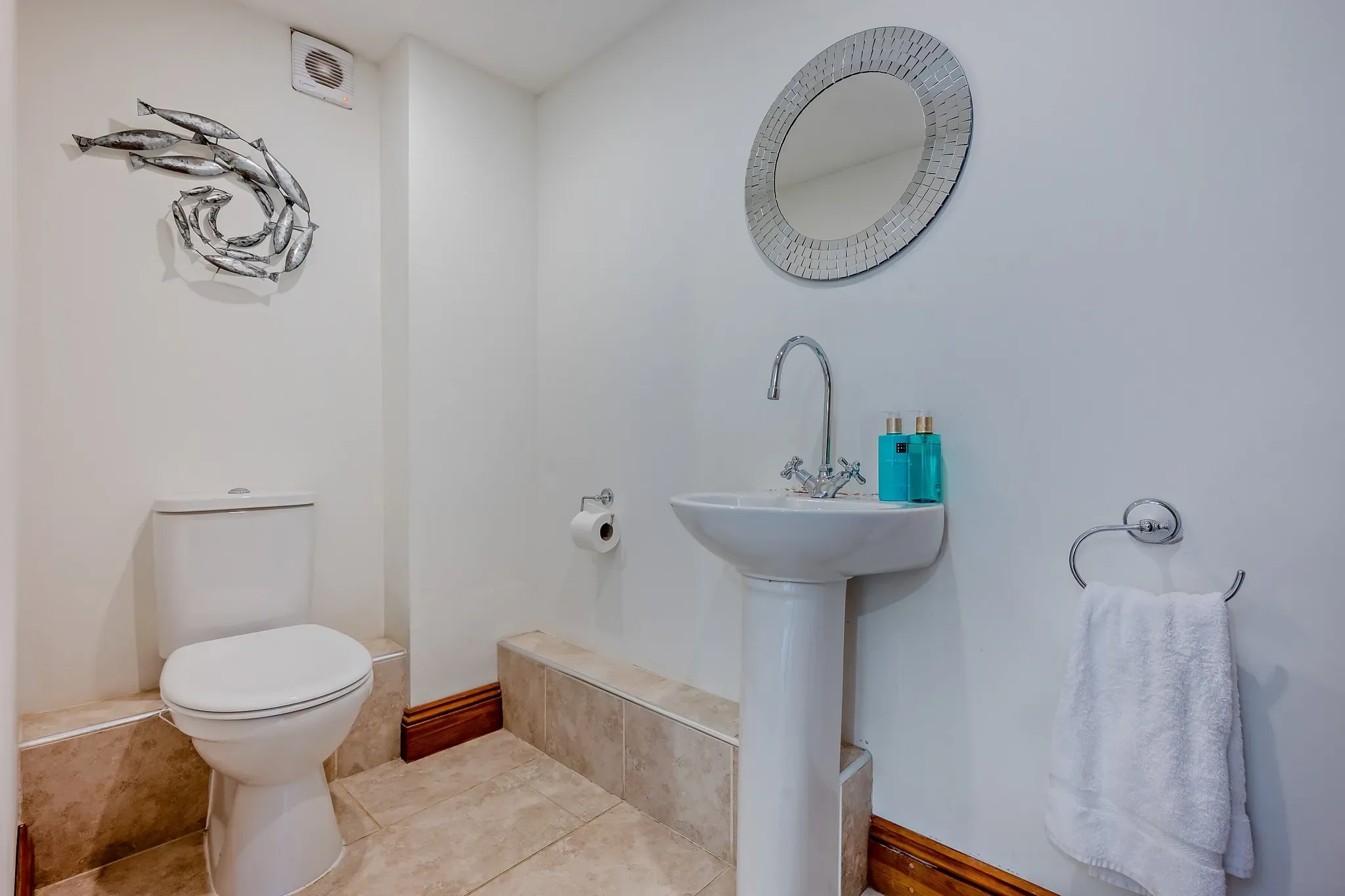 Middle Hill ground-floor cloakroom with pedestal basin, WC, round mosaic mirror, and a silver fish wall sculpture.