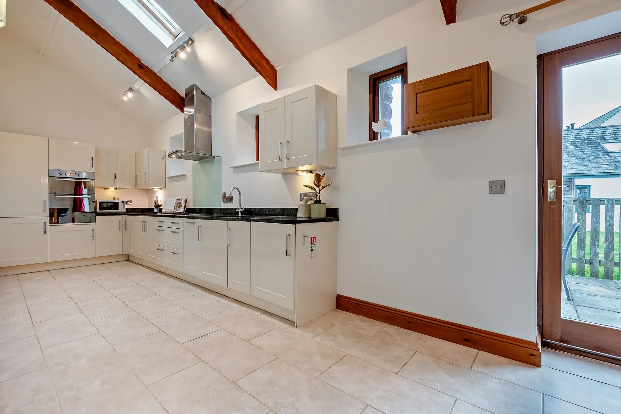 Middle Hill fully equipped kitchen with cream shaker units, dark granite worktops, vaulted ceiling with oak beams, and patio door to outside.