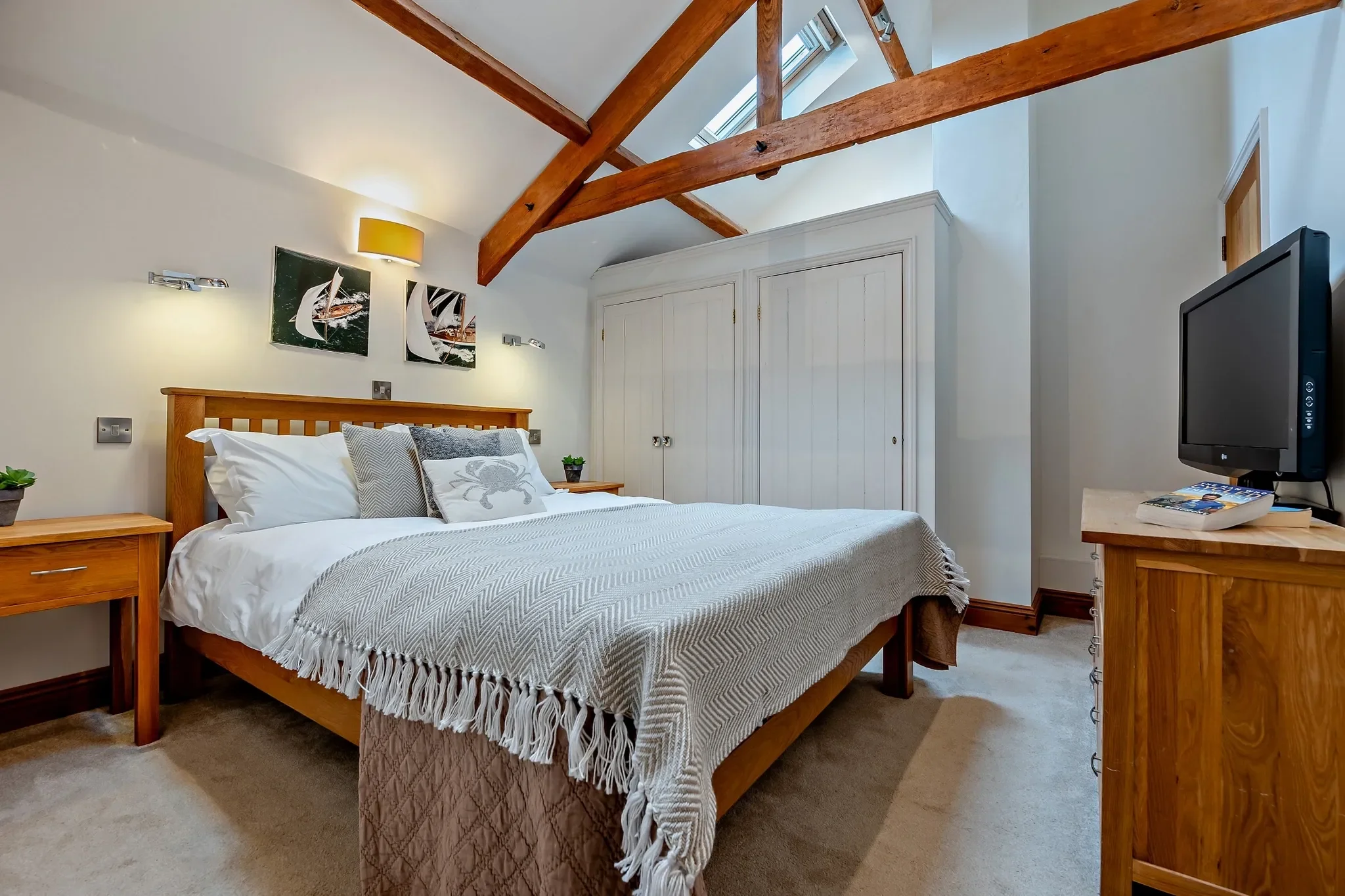 Middle Hill master bedroom with king-size bed, vaulted oak beams, built-in white wardrobes, and a flat-screen TV.