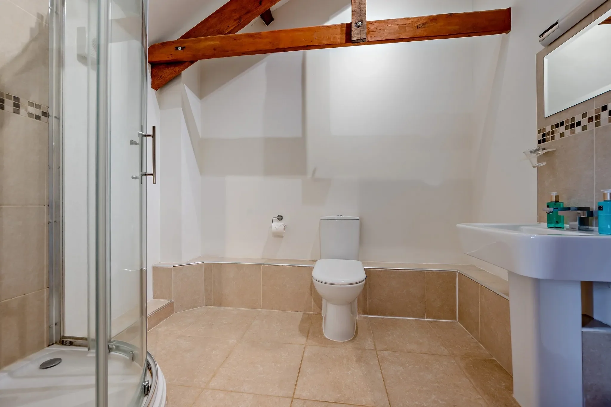 Middle Hill shower room featuring a corner quadrant enclosure, WC, pedestal basin, and exposed timber roof beams.