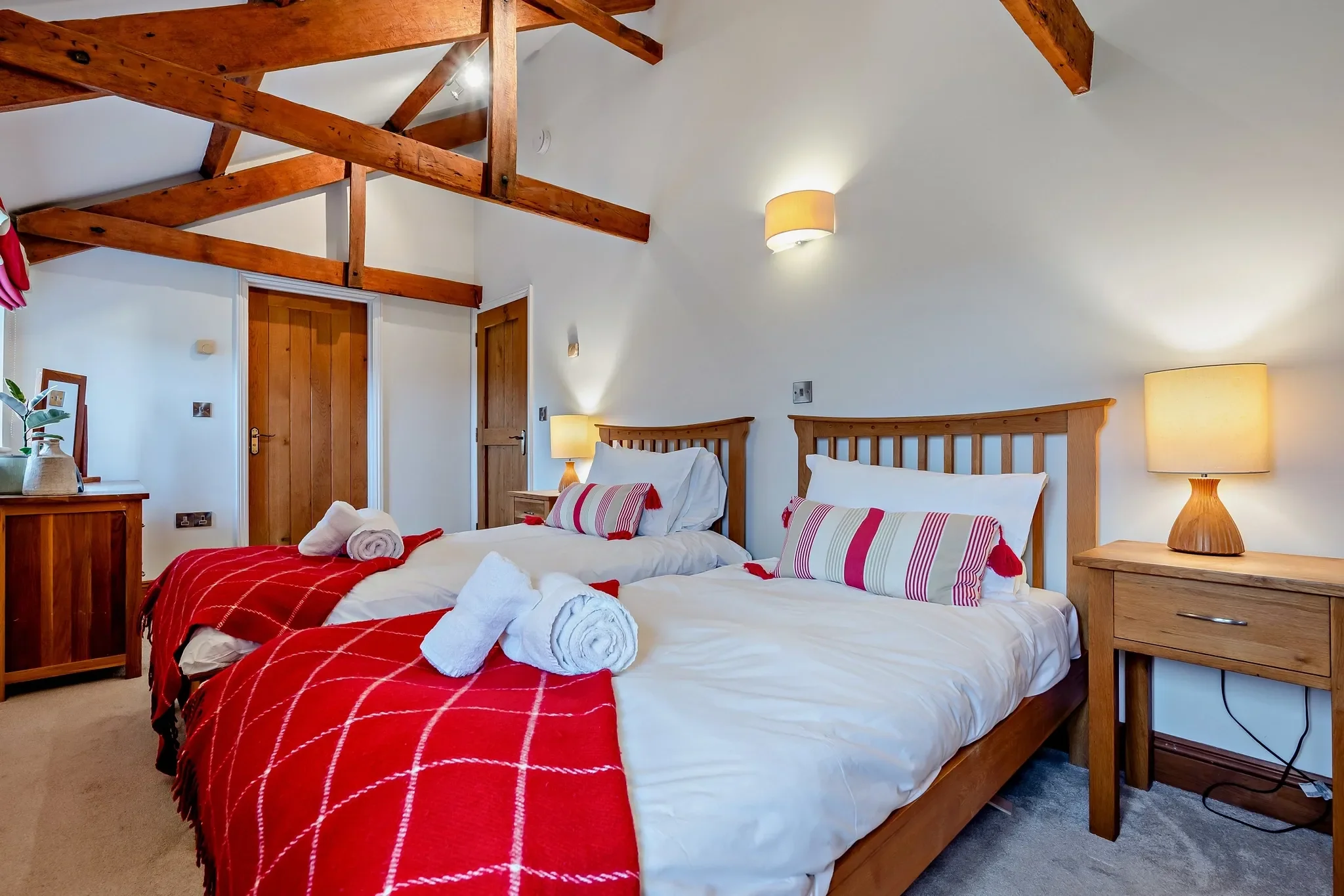 Middle Hill second bedroom in twin configuration, with two single beds dressed in red throws beneath vaulted oak rafters.