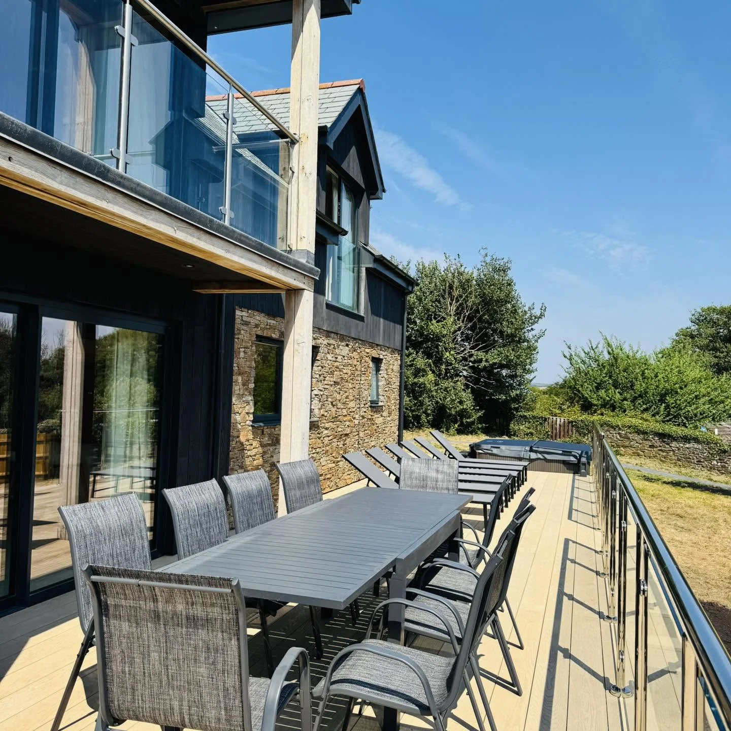 The deck at Nan's House, laid with a long outdoor dining table, sun loungers and the hot tub beyond