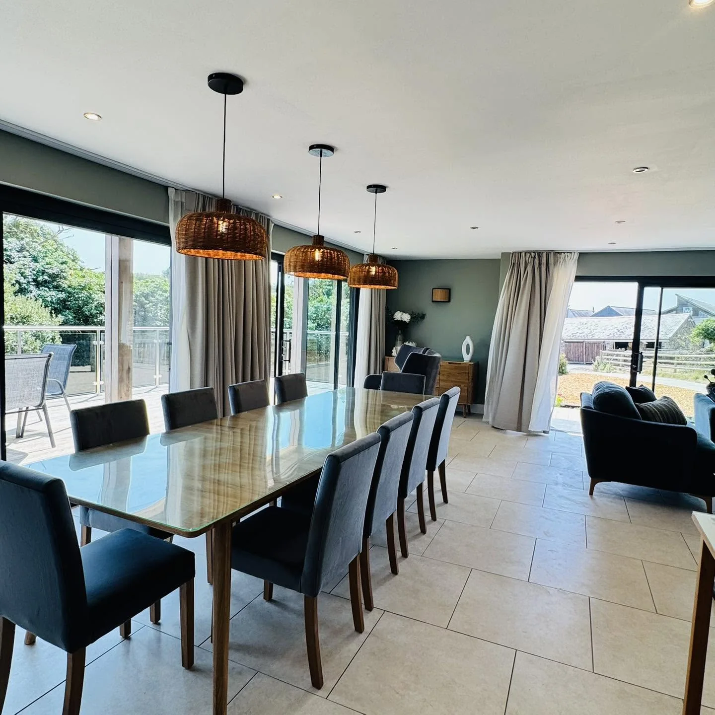 The dining table at Nan's House set under rattan pendants, open to the living area and the deck