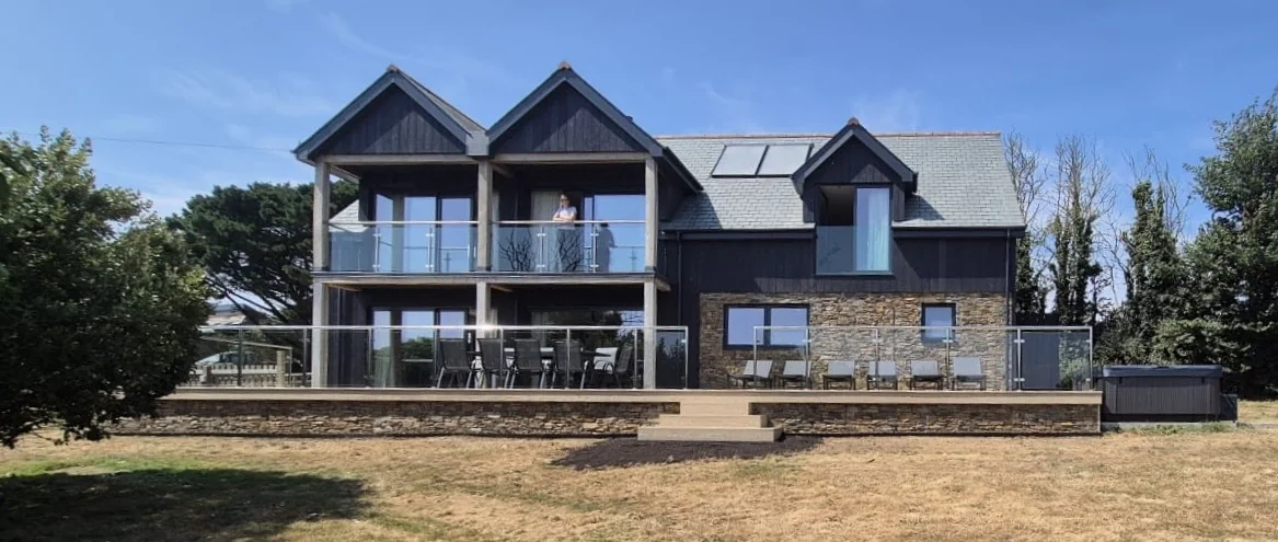 The full rear elevation of Nan's House, with balconies, a wide deck, outdoor dining and the hot tub to one side
