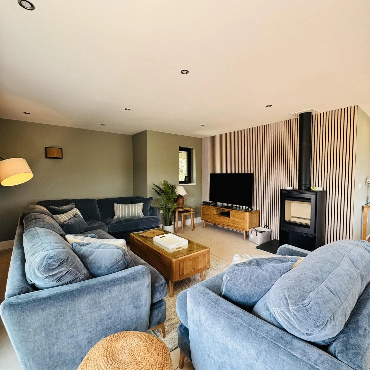 The living room at Nan's House, with deep velvet sofas, a wood-burning stove and a slatted timber wall