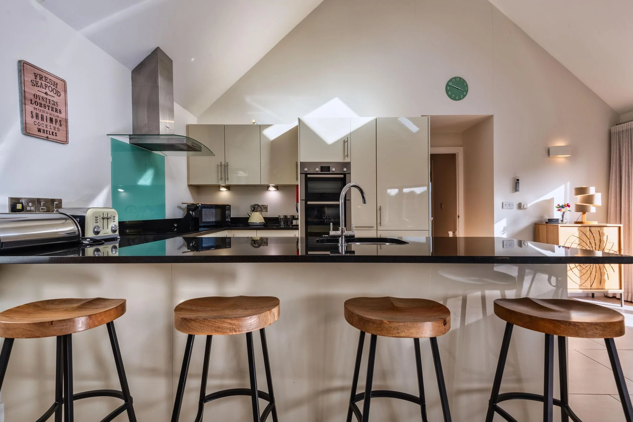 Nettlecoombe kitchen and dining zone viewed from the breakfast bar, with the lounge and wood-burner beyond.