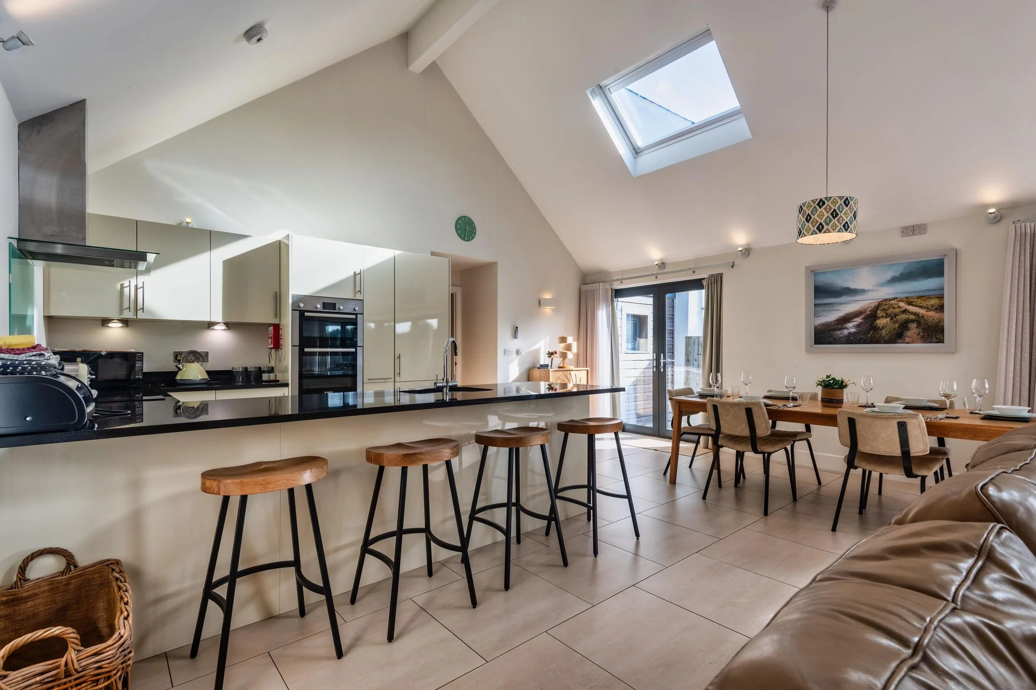 Nettlecoombe kitchen with gloss cream units, teal splashback, double oven, extractor and black granite breakfast bar.
