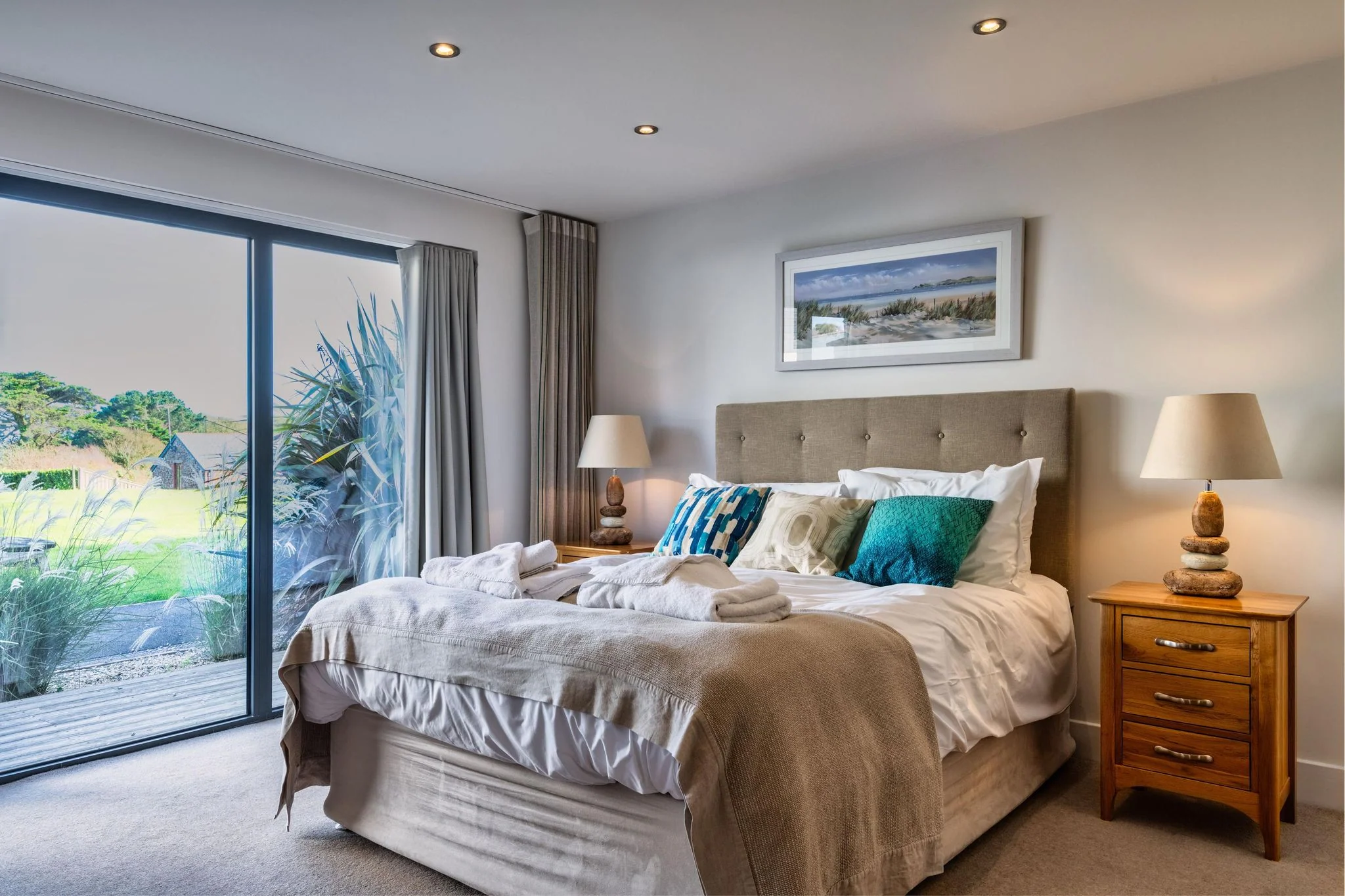 Nettlecoombe master bedroom showing the king-size bed with teal cushions and the ensuite bathroom doorway beyond.