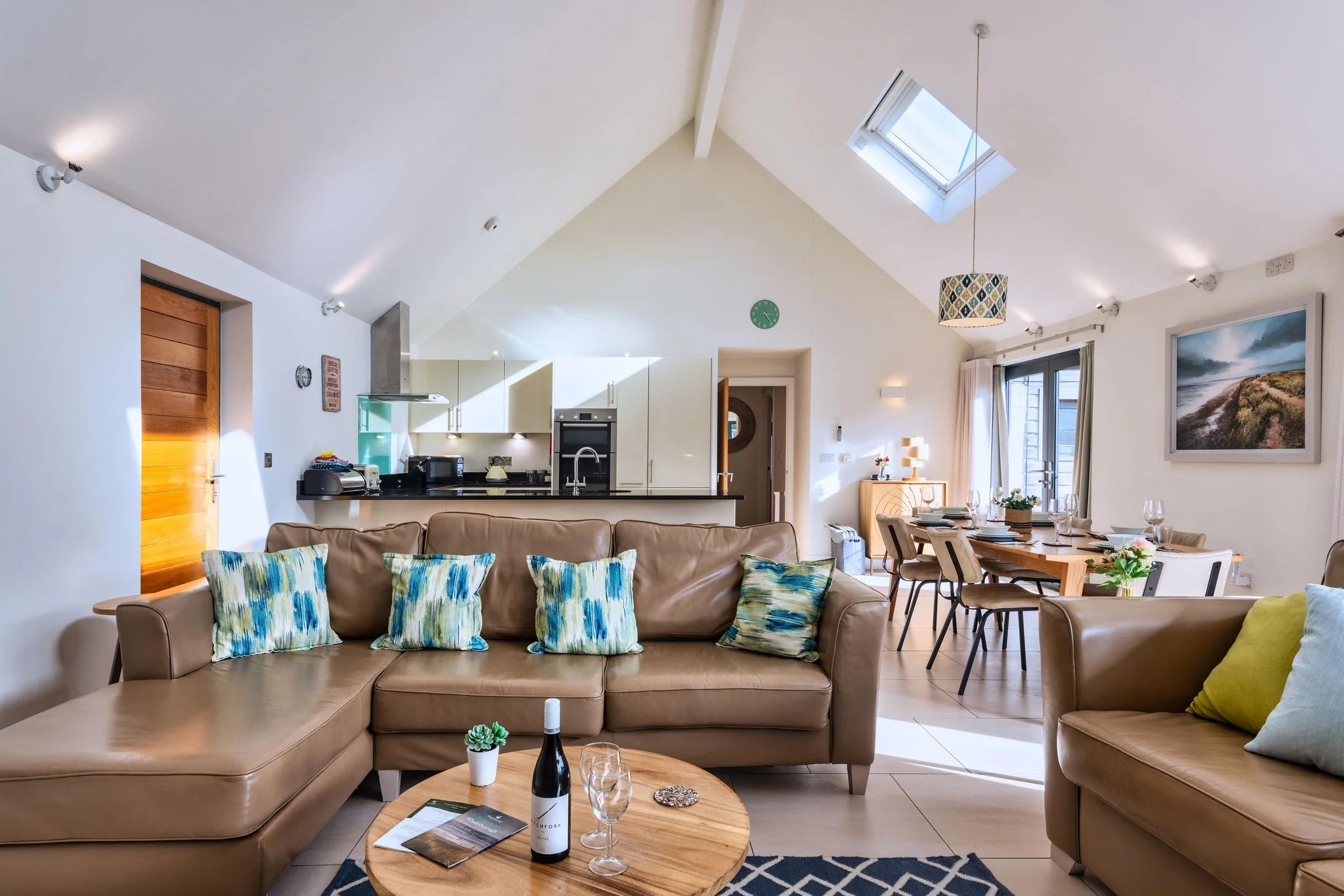 Nettlecoombe open-plan living space showing the kitchen, dining table and lounge under a vaulted skylit ceiling.