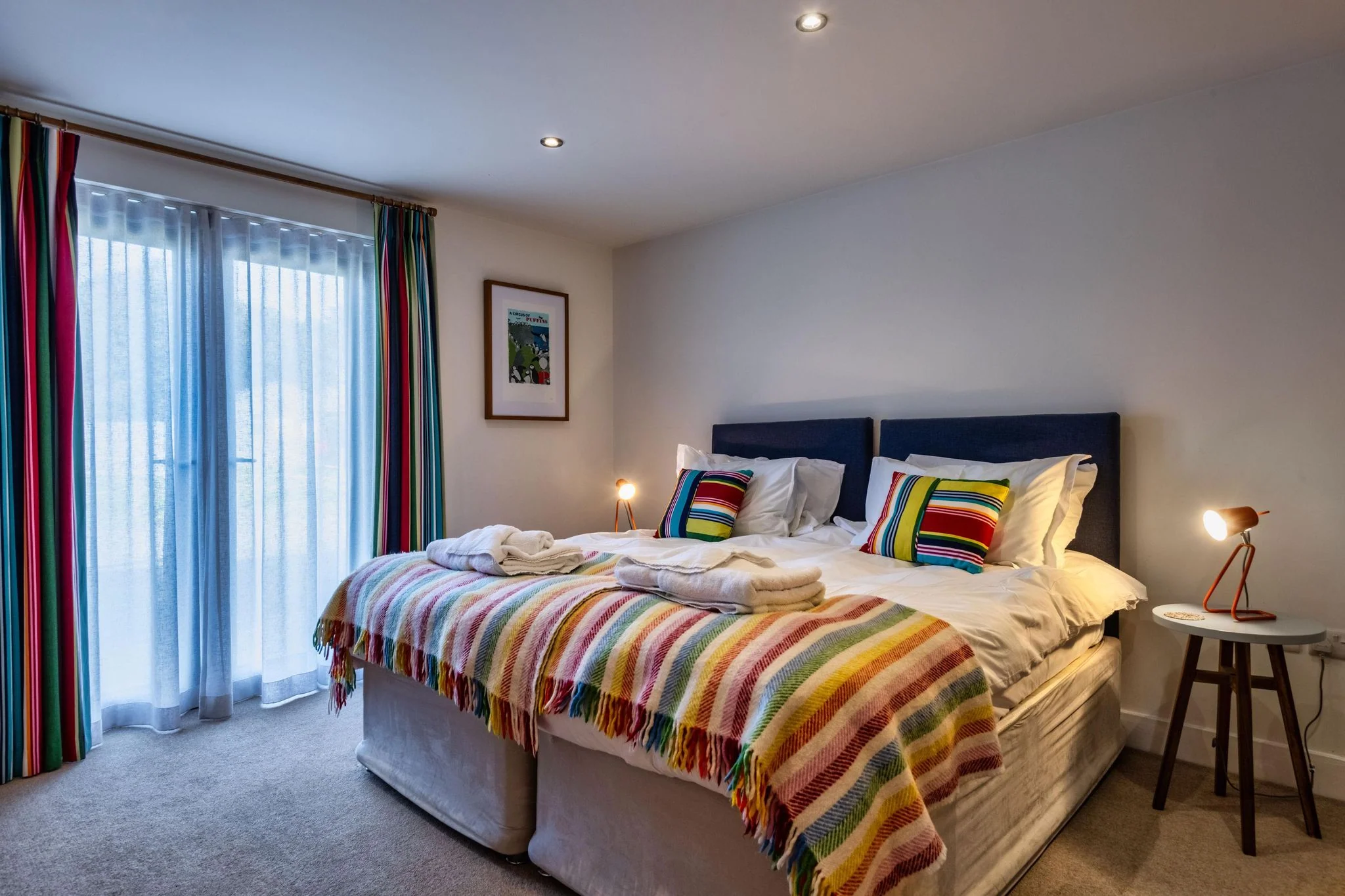 Nettlecoombe second double bedroom with a colourful striped bed throw and walk-in shower enclosure visible through the doorway.