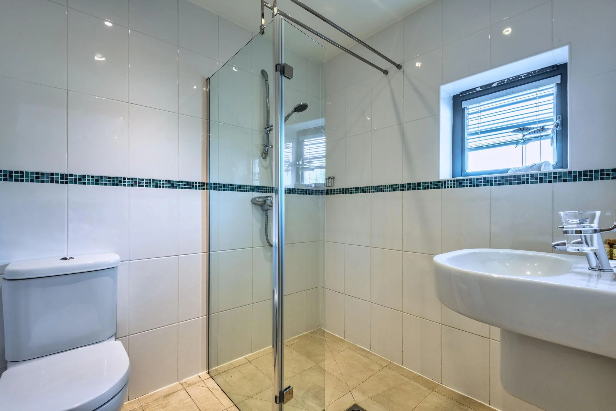 Nettlecoombe second shower room with a walk-in glass enclosure, WC, wall-hung basin and teal mosaic tile stripe.