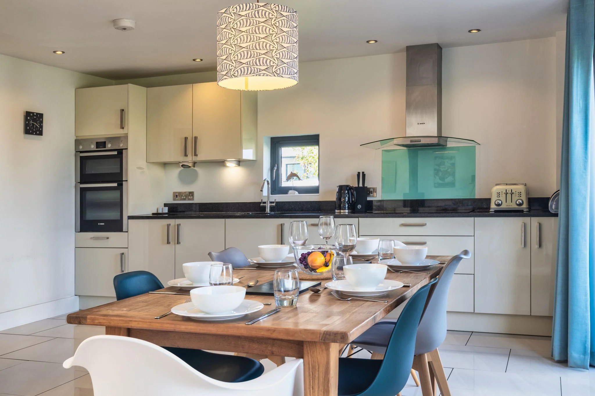 Sheep's House kitchen-diner with cream fitted units, integrated double oven, teal splashback, and a large wooden dining table set for six.