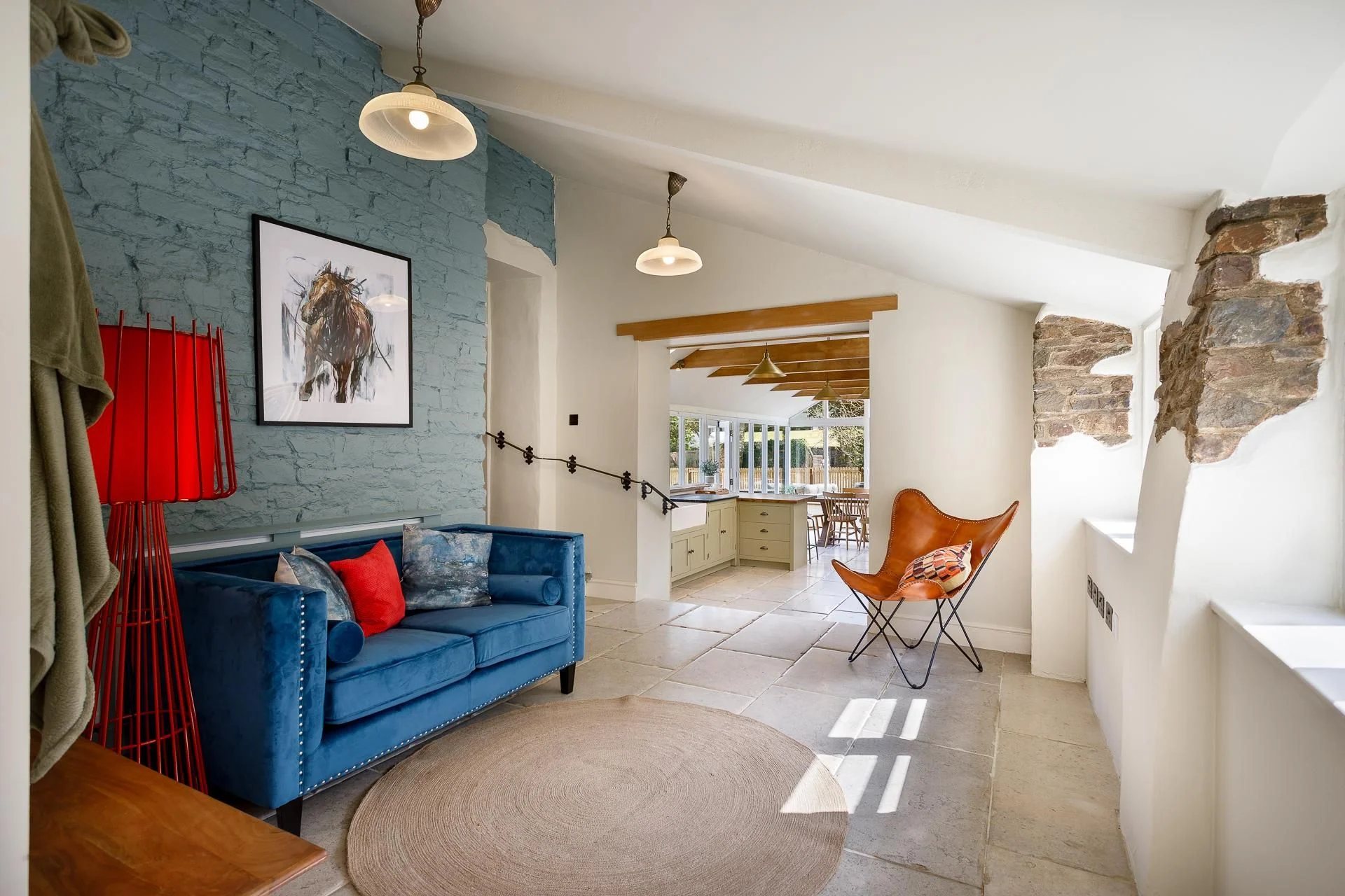 The Farmhouse entrance hall with exposed blue painted stone wall, velvet sofa, and an open view through to the kitchen beyond.
