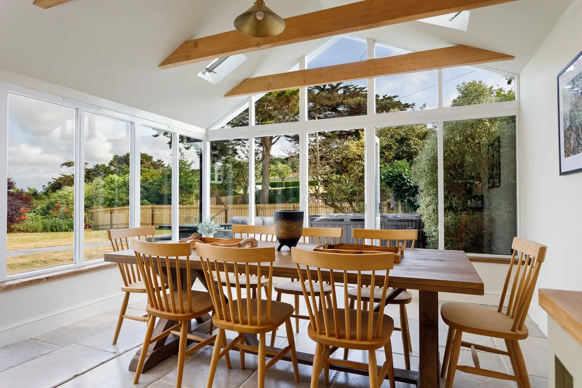 The Farmhouse garden-room dining area with a large oak table seating eight, surrounded by panoramic glazed walls overlooking the lawn.