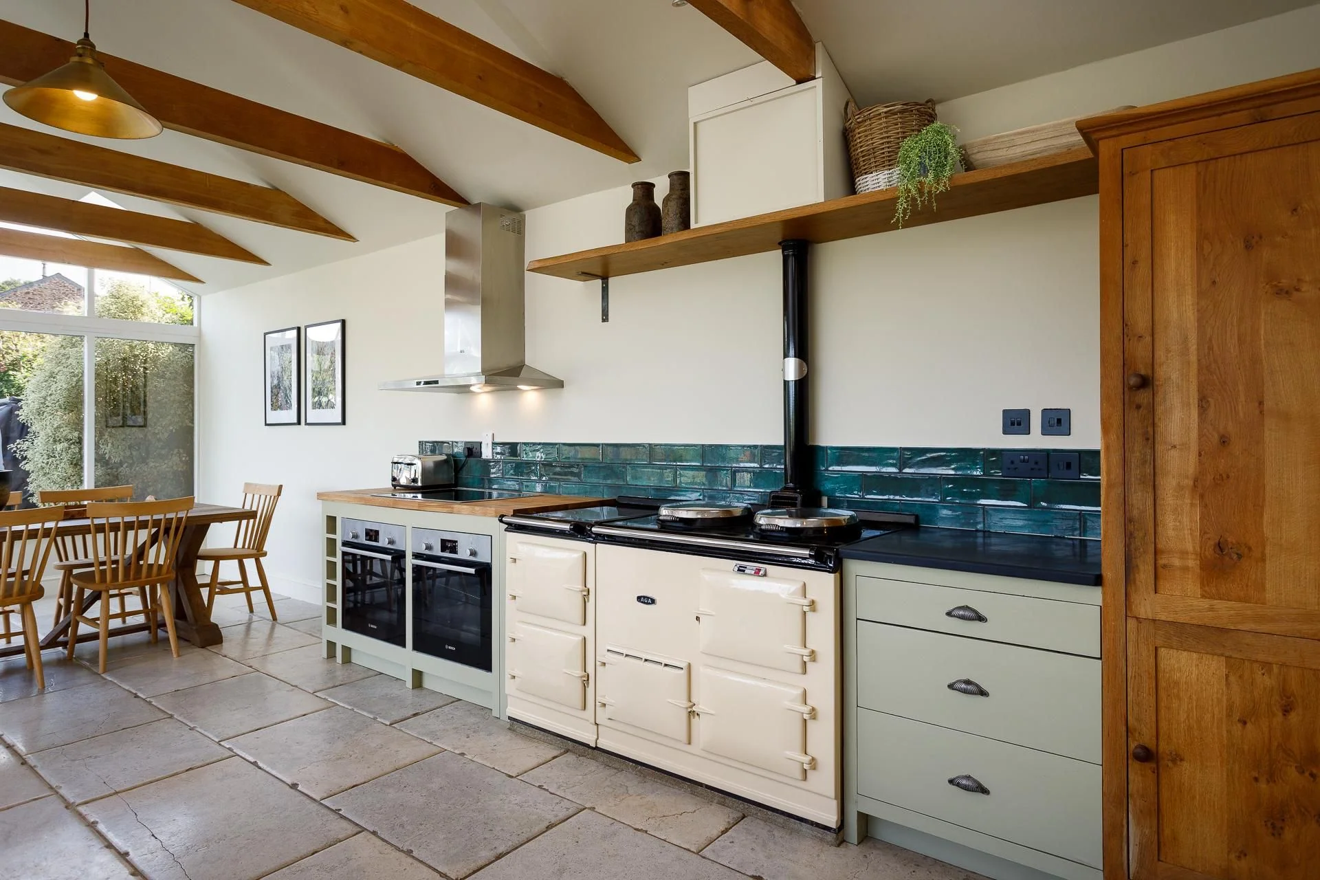 The Farmhouse kitchen showing the cream range cooker beneath teal metro tiles with open oak shelving above.