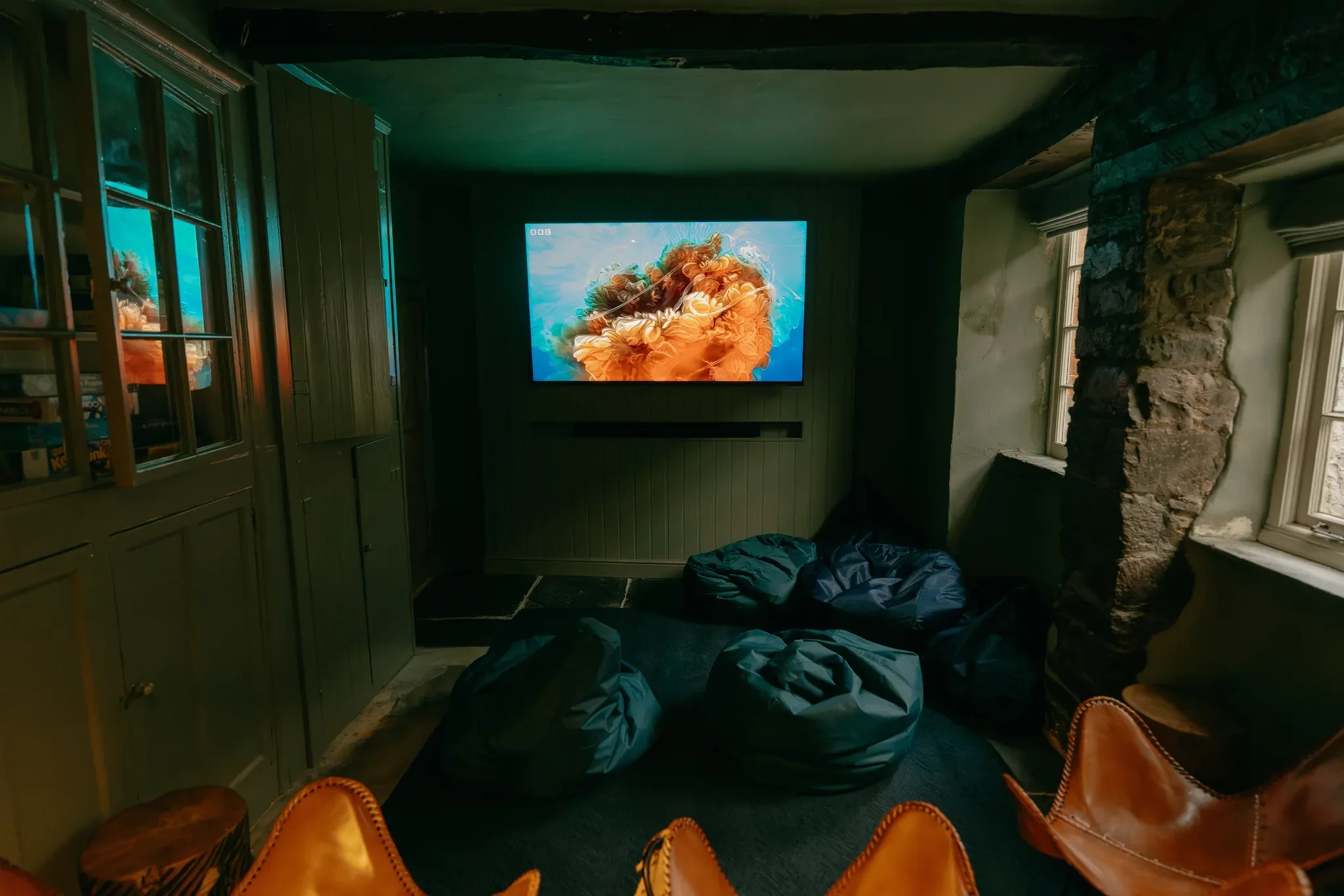The Farmhouse snug cinema room with a wall-mounted screen, bean bags and leather chairs set within stone walls.