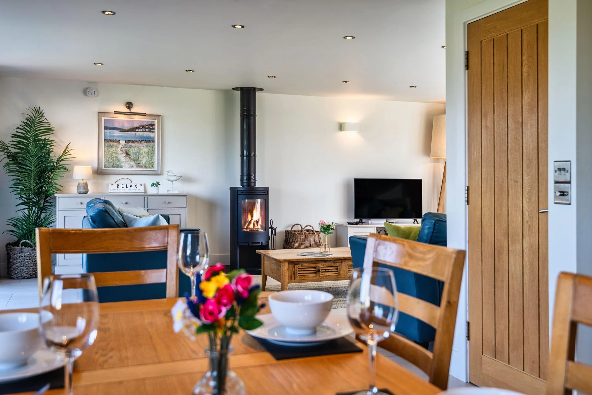 Trevelyan dining table set for six with wine glasses looking through to the wood-burner and lounge beyond.
