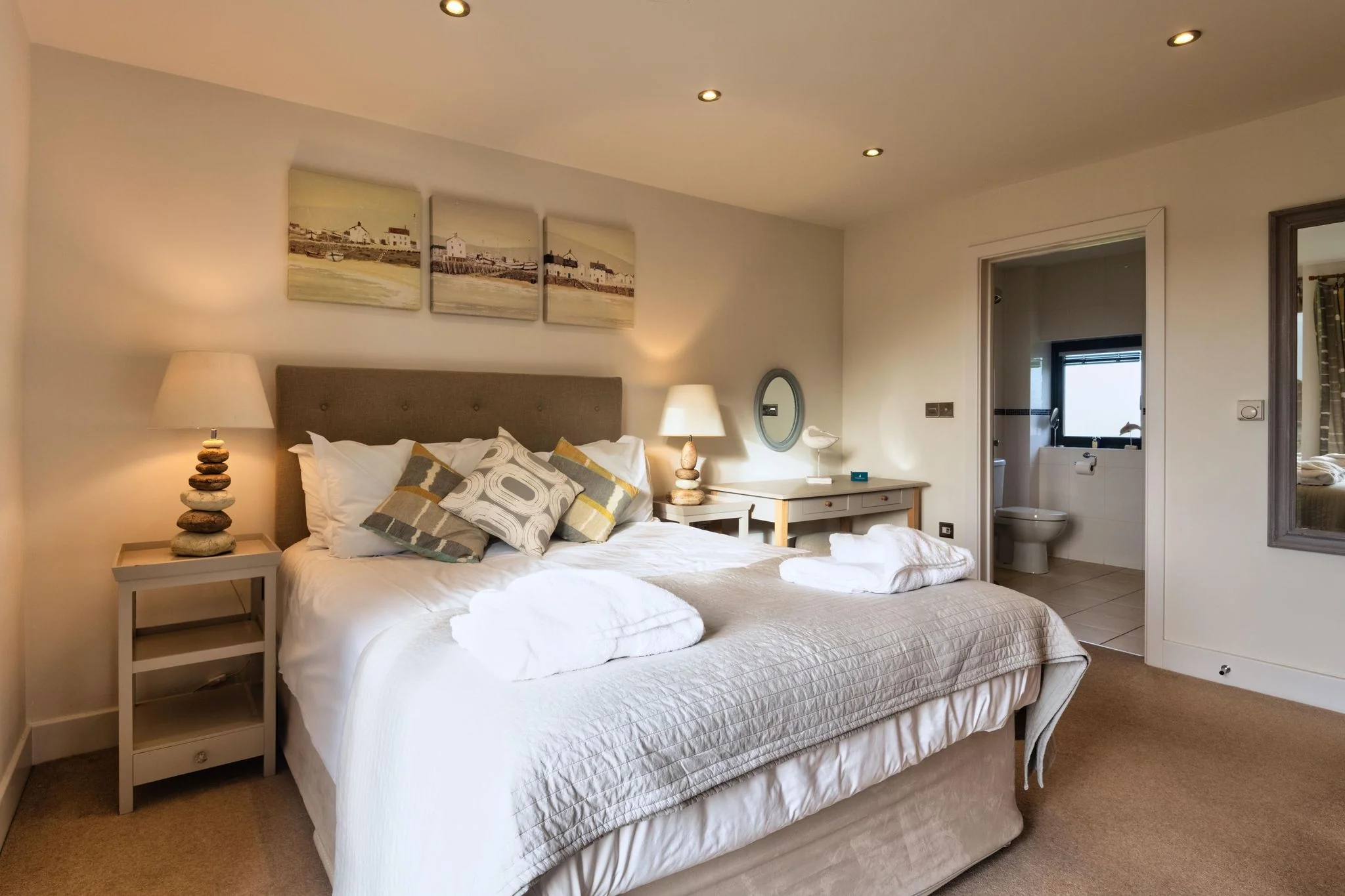 Trevelyan double bedroom with king-size bed, coastal artwork above the headboard and en-suite bathroom visible beyond.