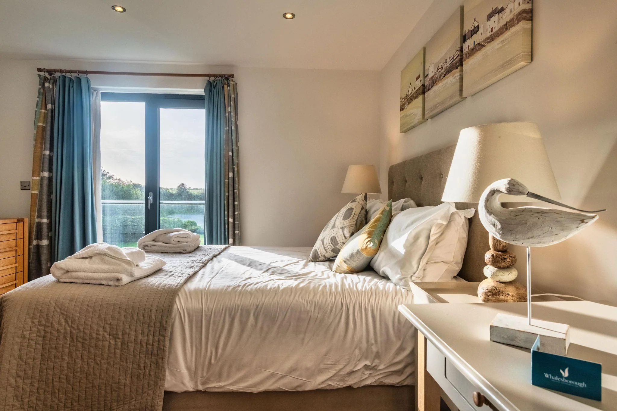 Trevelyan double bedroom with king-size bed, teal curtains and French doors framing a lake and estate view.