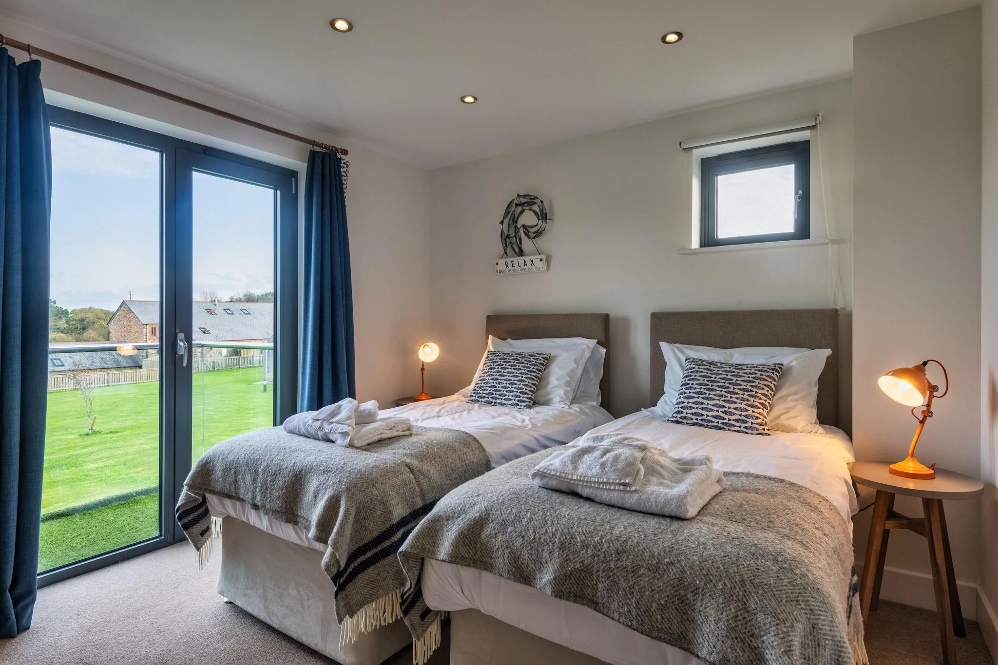 Trevelyan twin room with two single beds, teal curtains and wide garden-facing glass doors flooding the room with light.