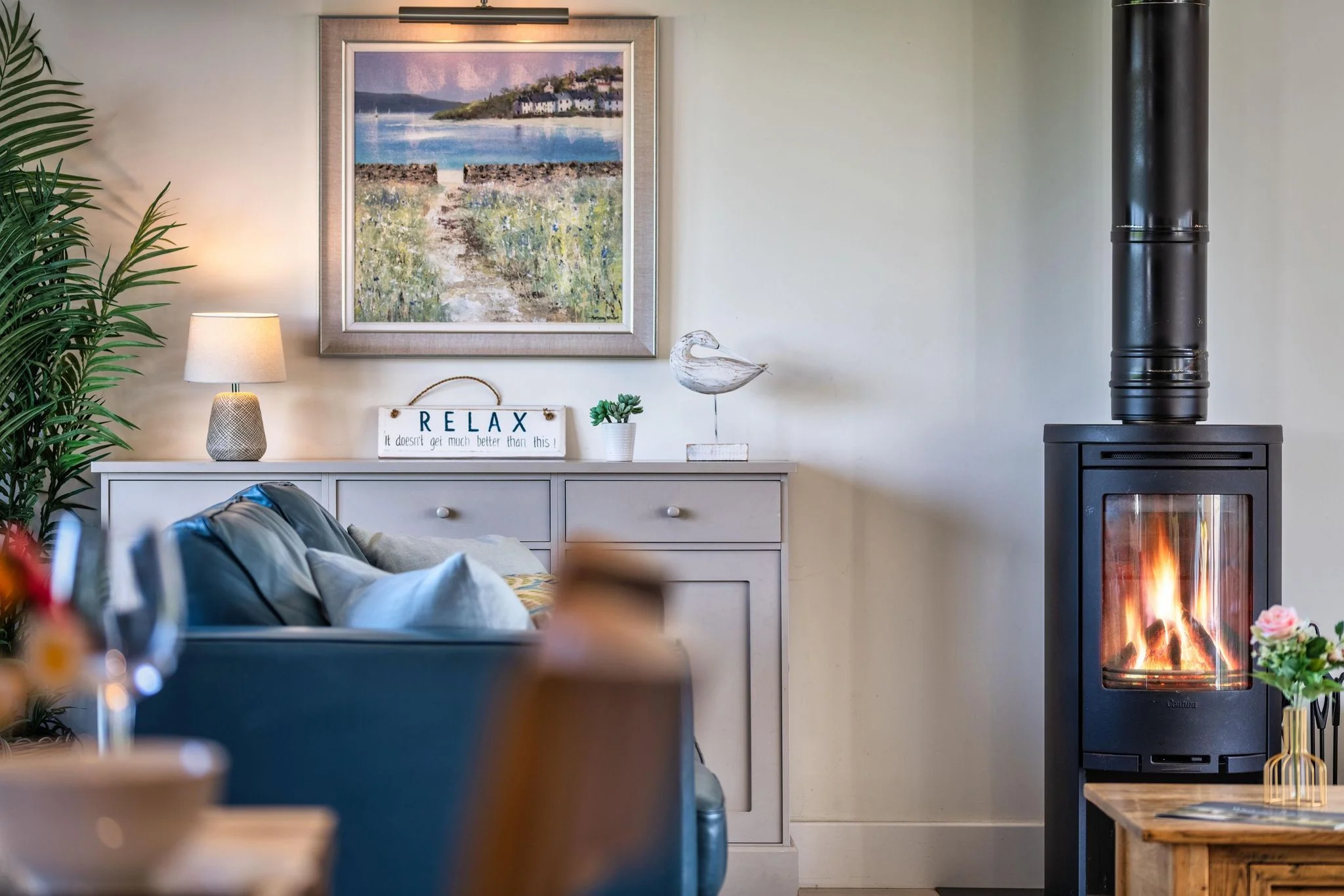 Trevelyan blazing wood-burning stove beside the sideboard displaying coastal artwork and a seabird ornament.