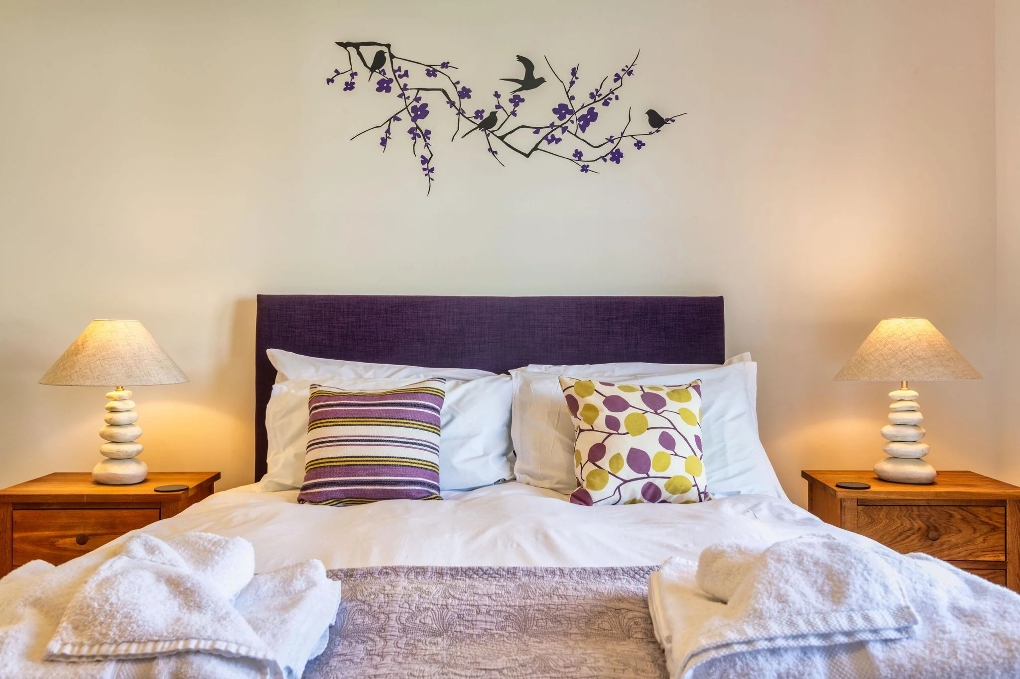 Venners master bed close-up showing crisp white linen, striped cushions and decorative bird-branch wall art above.