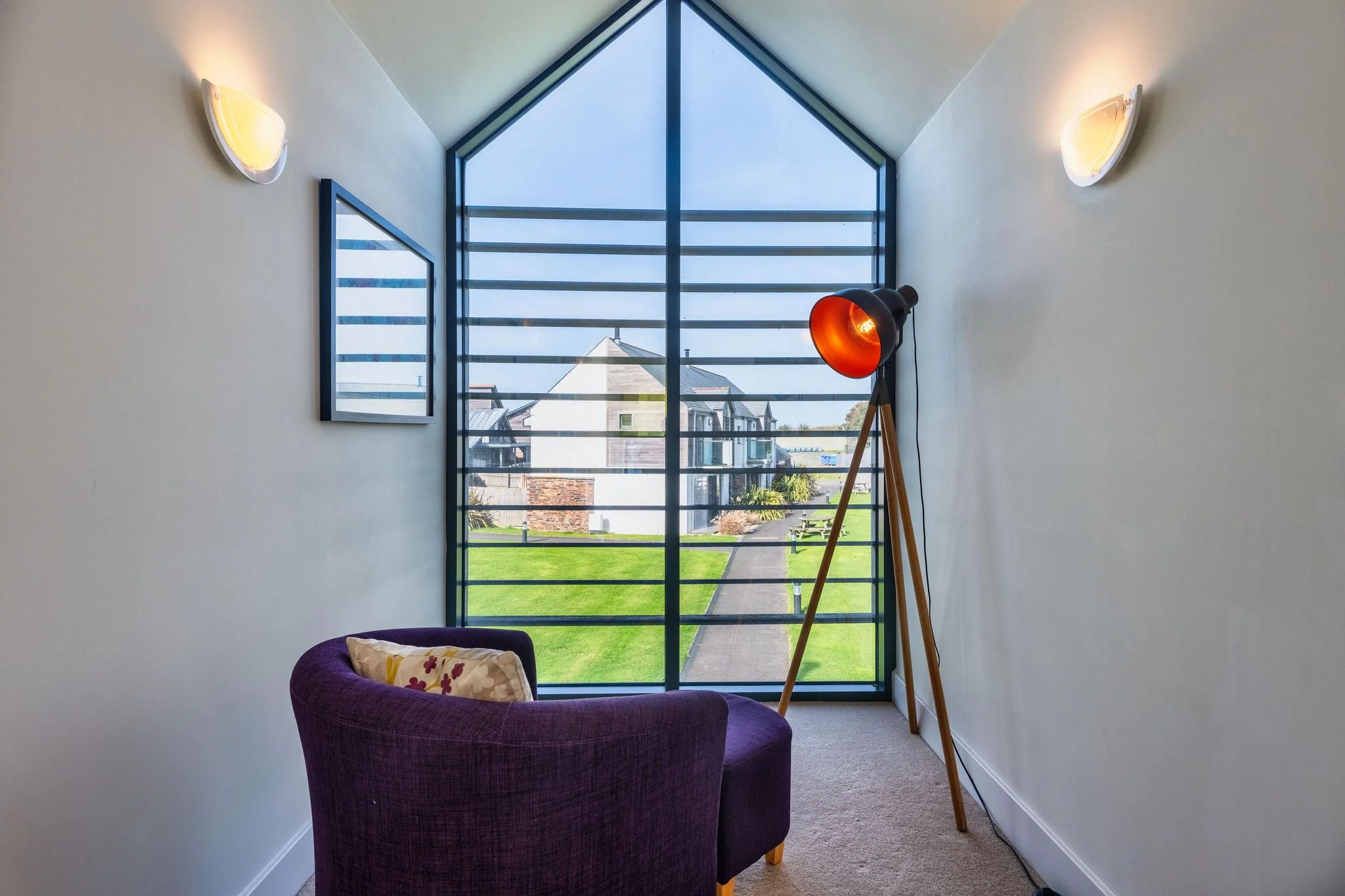Venners mezzanine reading nook with a floor-to-ceiling gable window, armchair and tripod lamp overlooking the estate.