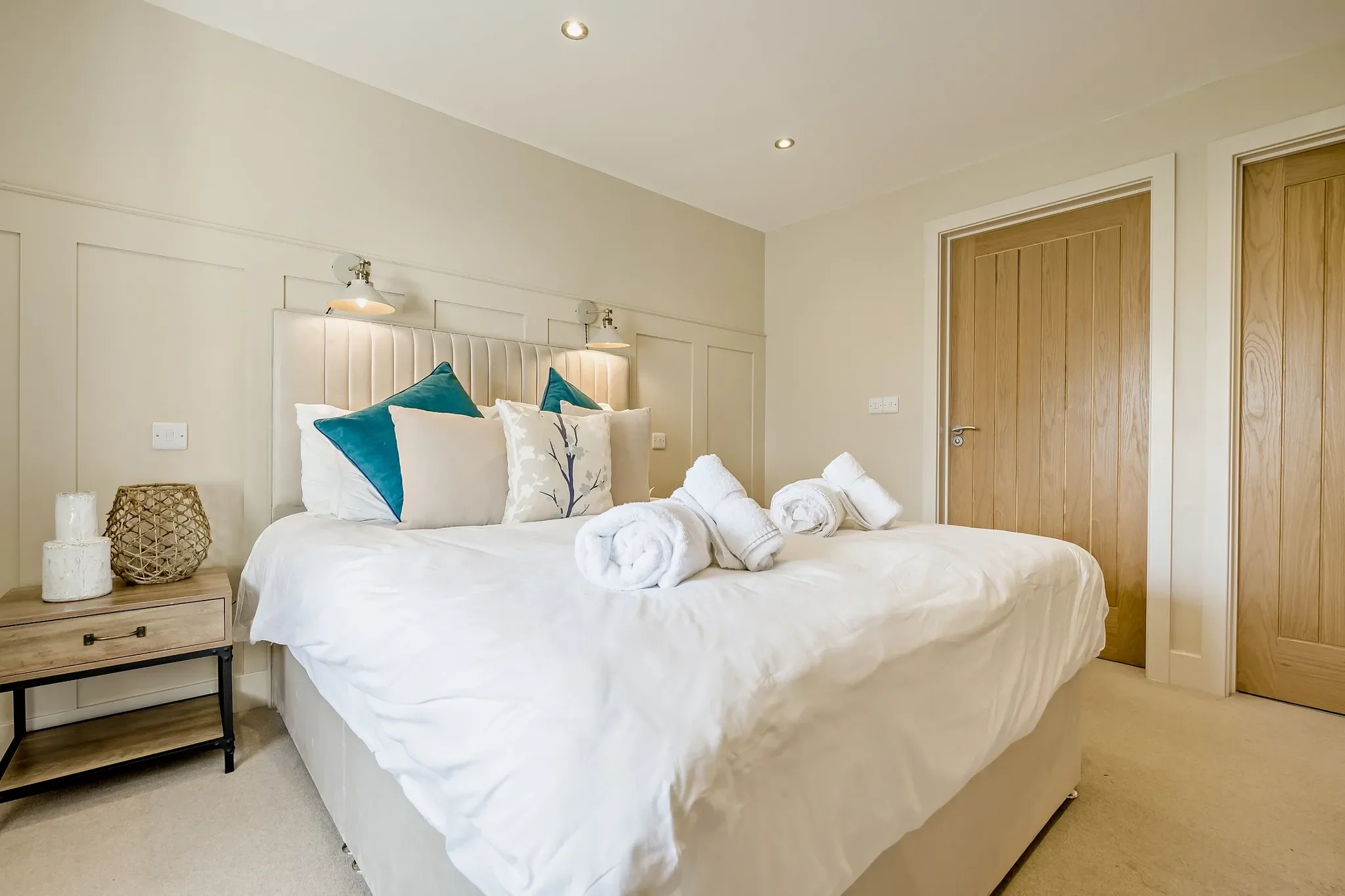 Warrens second double bedroom with king-size bed, teal cushions, twin wall lights and oak door to ensuite.