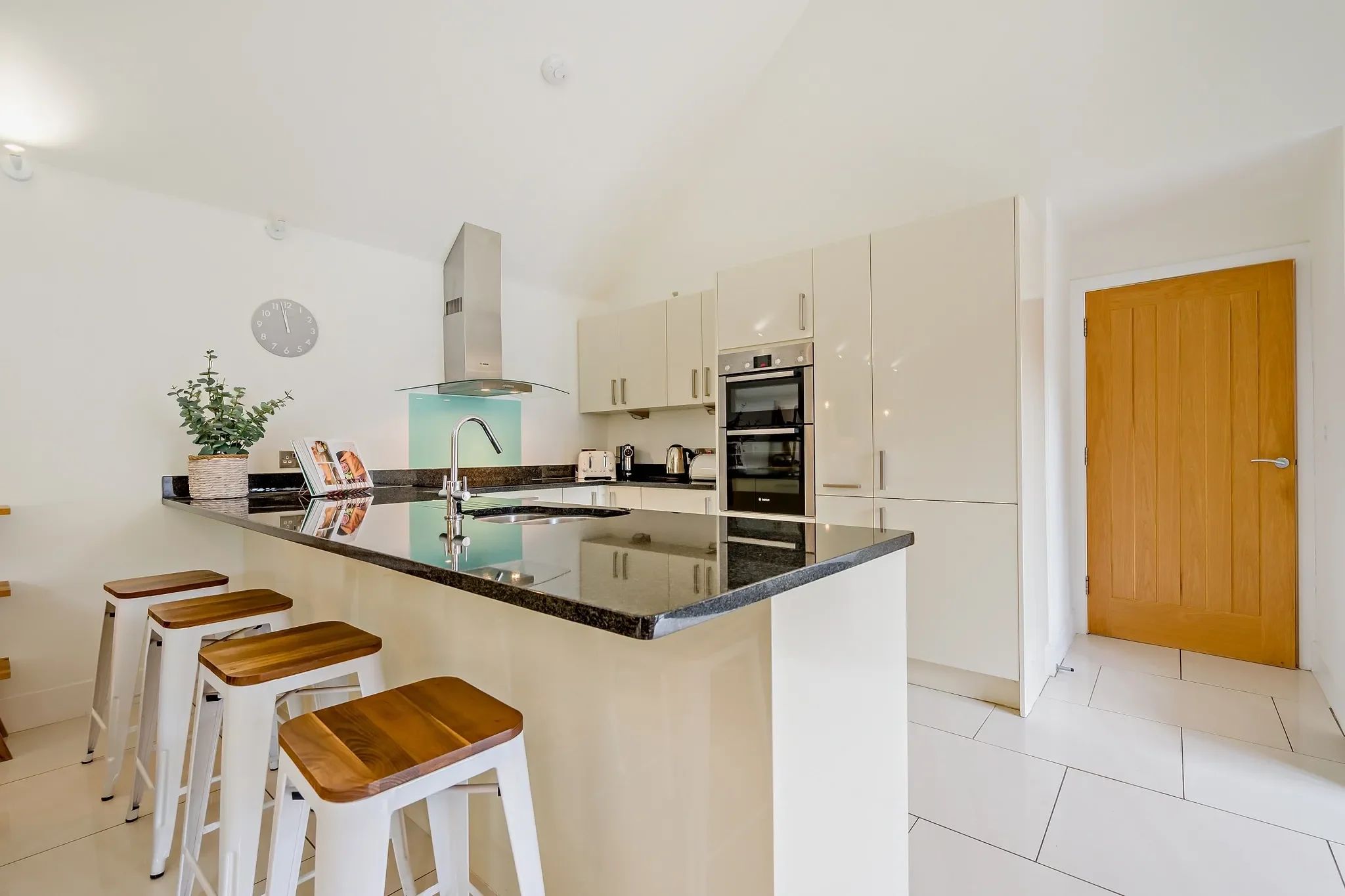 Warrens kitchen with high-gloss white units, granite island breakfast bar, double oven and teal glass splashback.