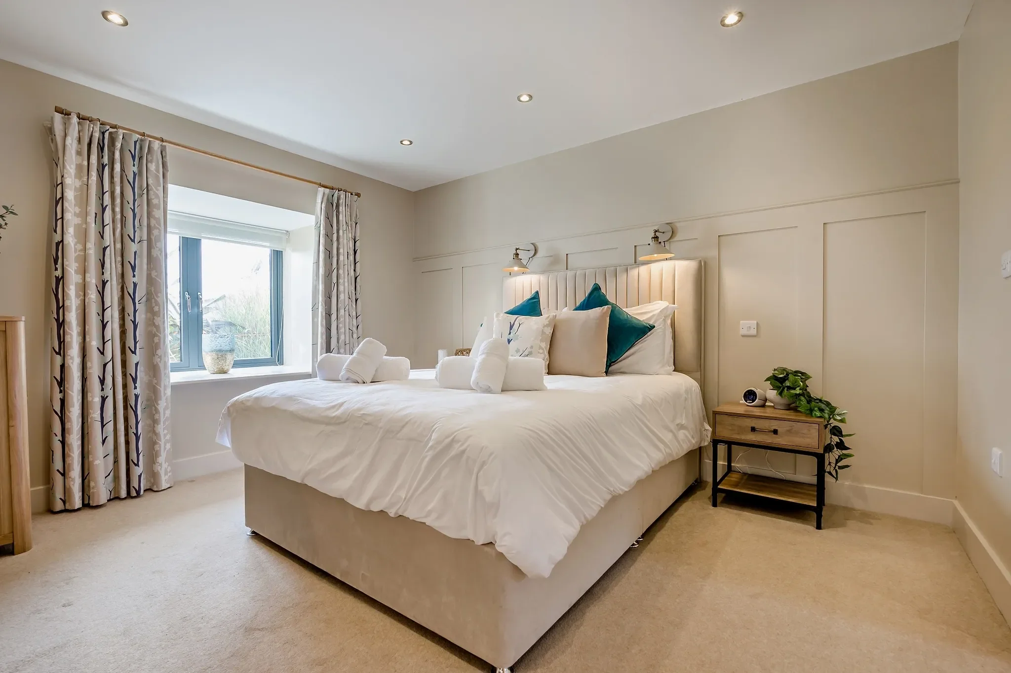 Warrens master bedroom with king-size bed, teal accent cushions, panelled headboard and garden-view window.