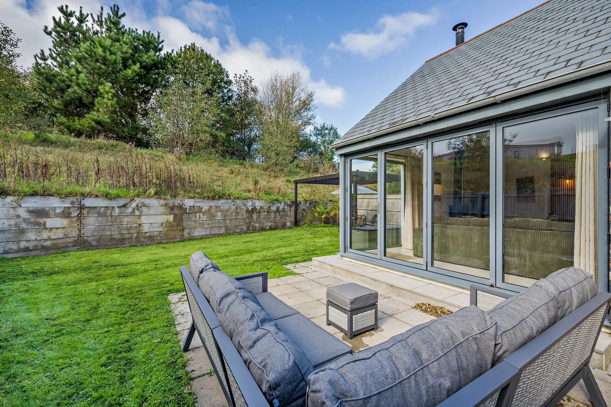 Warrens stone-paved terrace with outdoor sofa set and fire pit, overlooking the private lawned garden and wooded hillside.