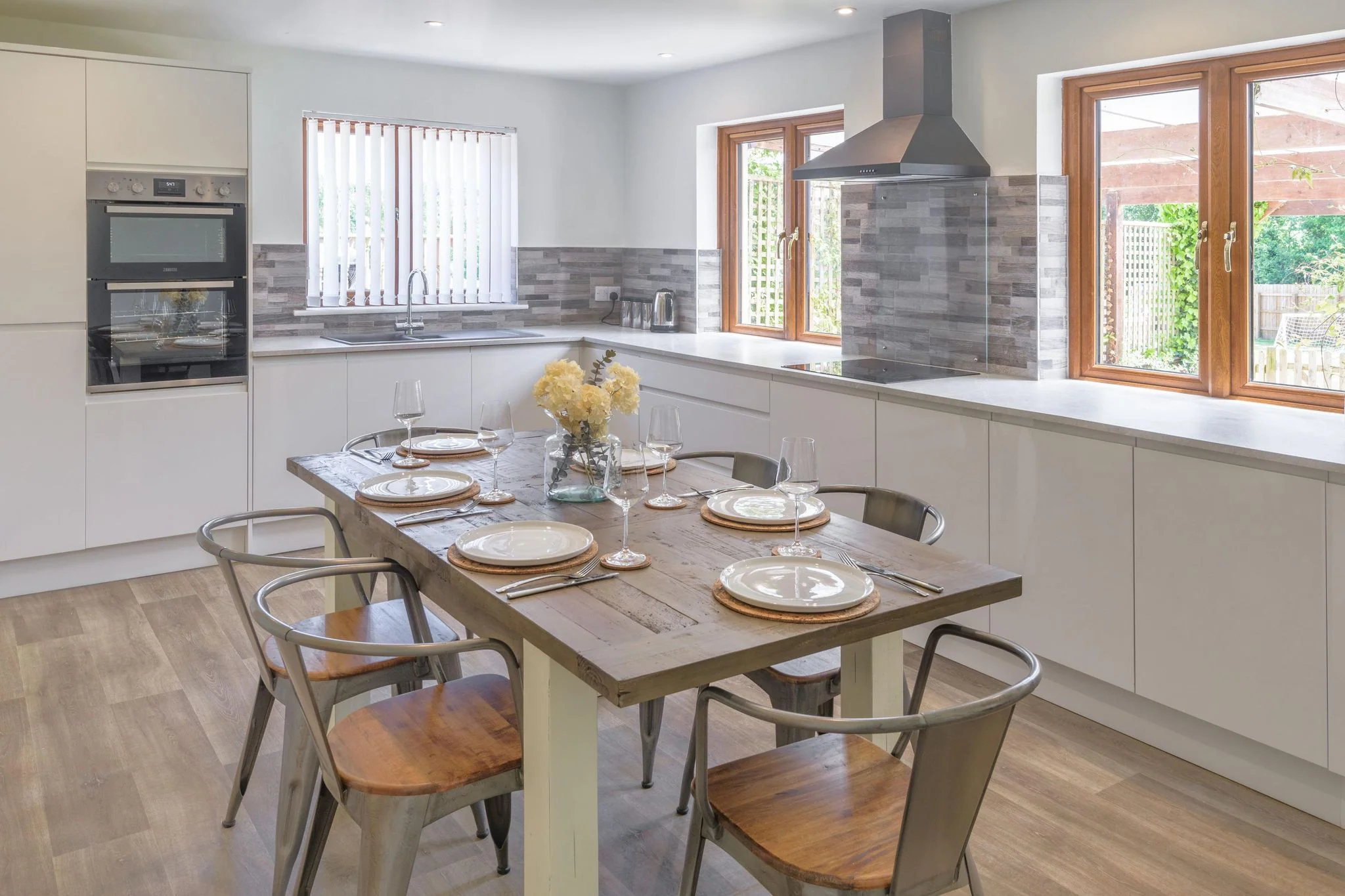 Windy Hills kitchen-diner close-up of the laid dining table with grey tile splashback and double oven behind.