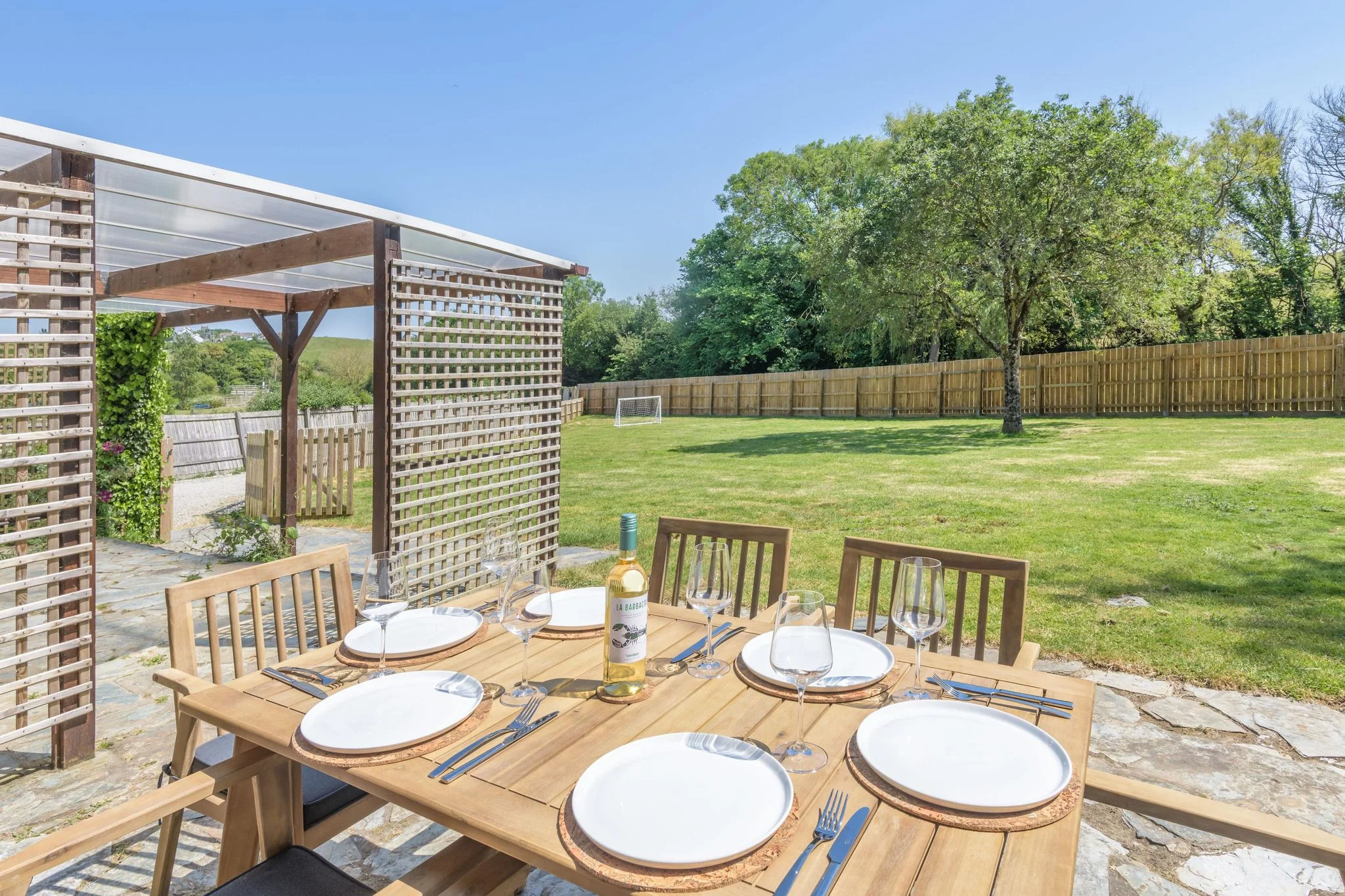 Windy Hills stone patio with a six-seat teak dining set dressed for al fresco dining, overlooking the lawned rear garden.