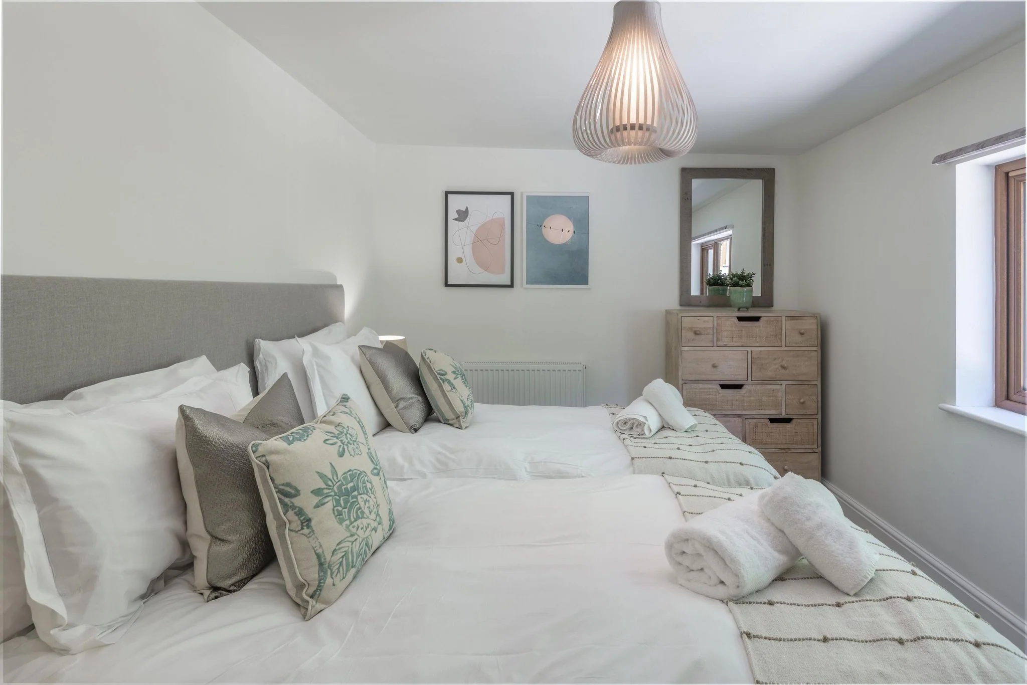 Windy Hills twin room with two single beds dressed in white linen, teal cushions, and a rustic wood chest of drawers.