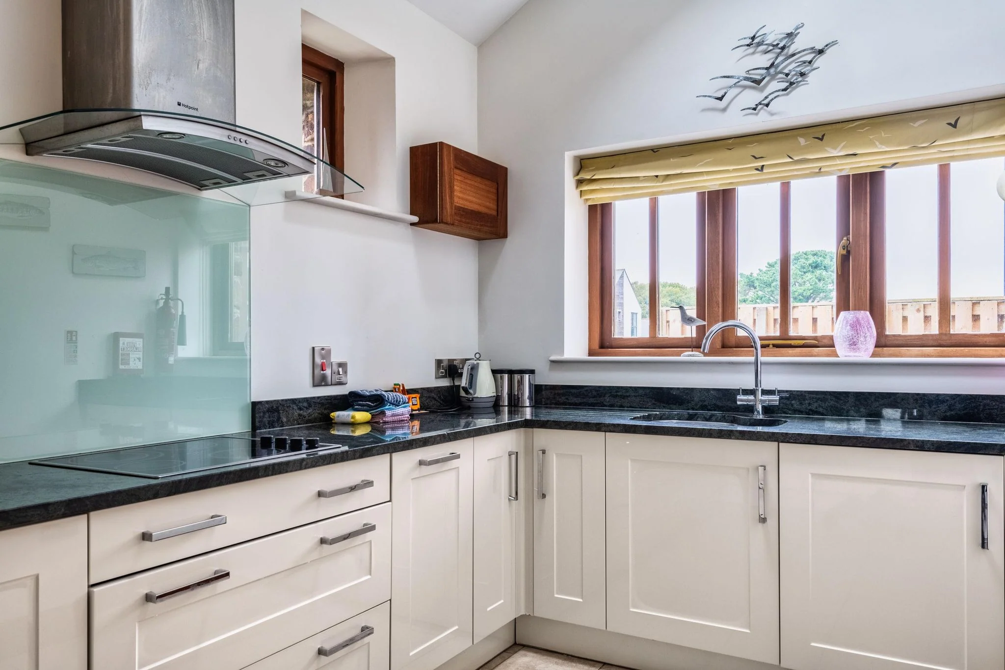 Woody Platt kitchen with cream shaker units, granite worktops, induction hob and glass splashback.