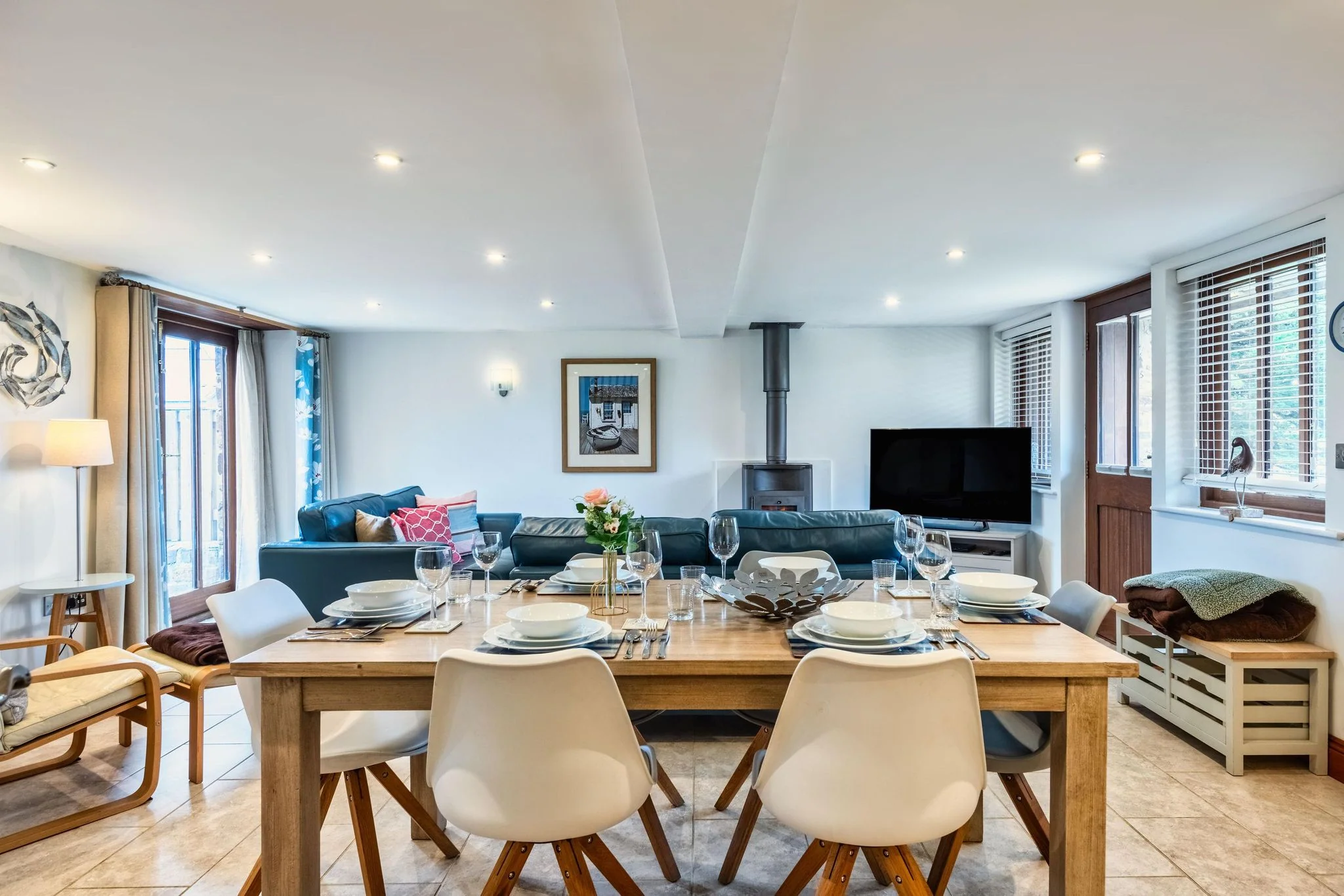 Woody Platt open-plan dining and living area with oak table set for six, leather sofas and log burner beyond.