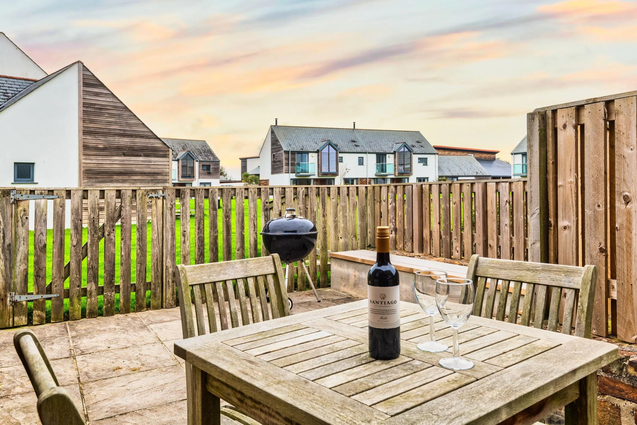Woody Platt private paved terrace with teak dining furniture, charcoal BBQ and estate views at sunset.