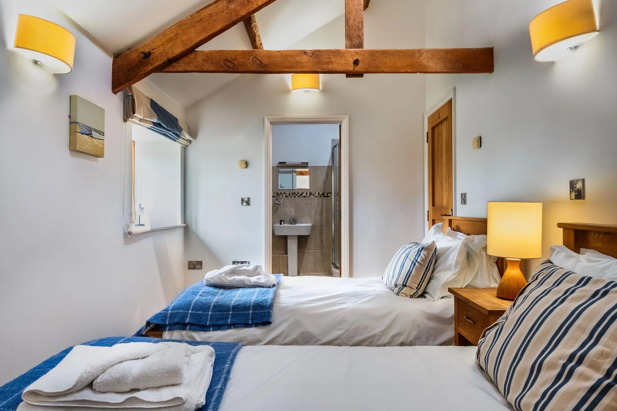 Woody Platt twin bedroom with vaulted oak-beam ceiling, blue tartan throws and ensuite visible through the doorway.