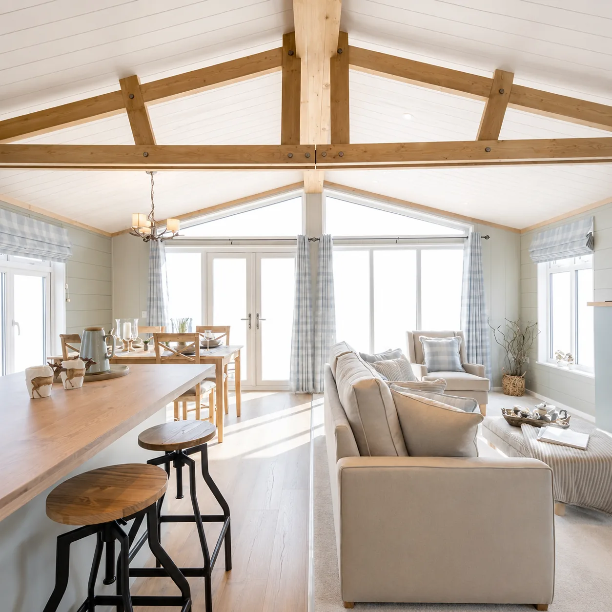 Open-plan living, dining and breakfast bar in the two-bedroom Gwithva lodge, under exposed roof trusses