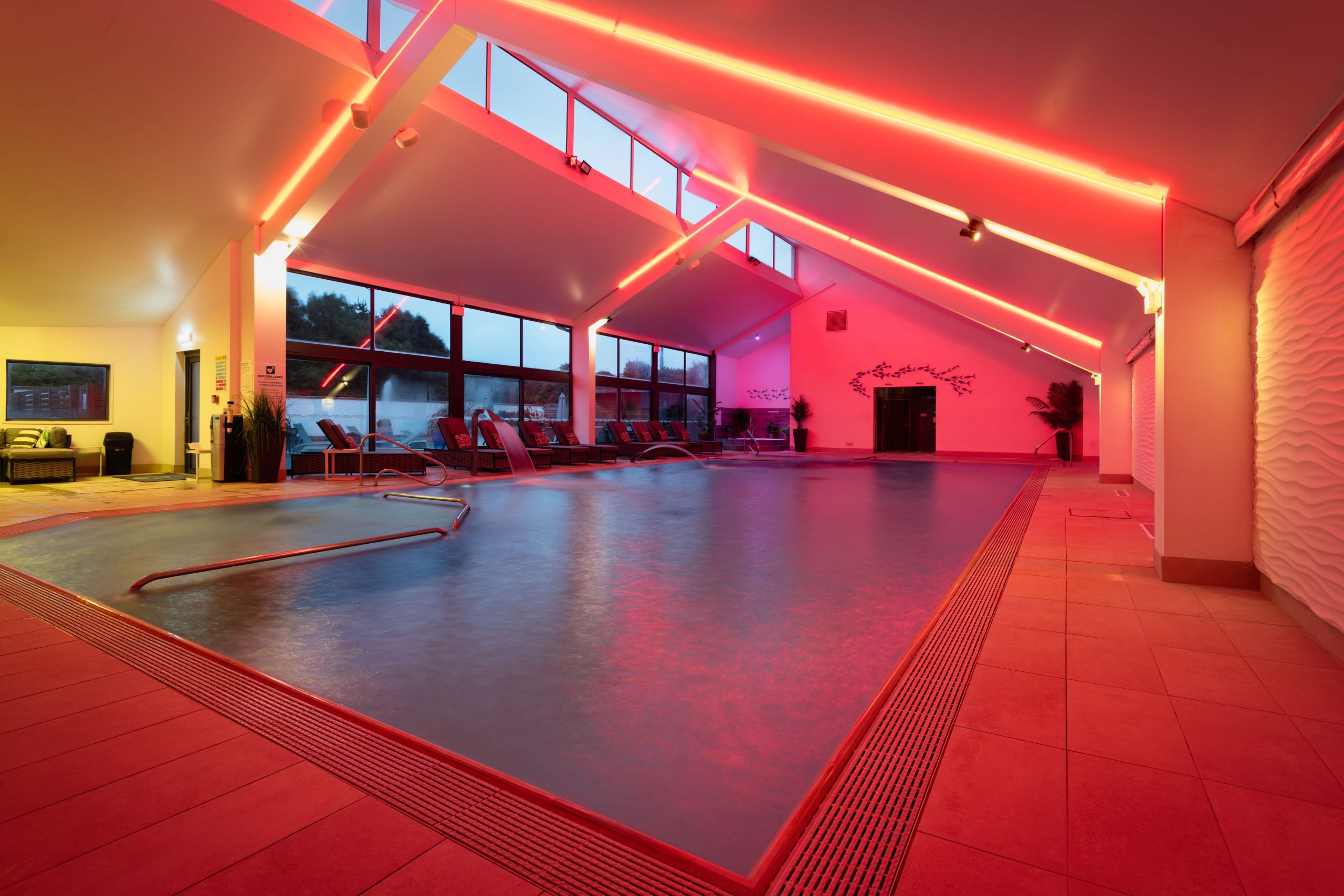 Indoor infinity pool under a pitched ceiling with mood lighting at The W Club, Whalesborough, Bude, Cornwall